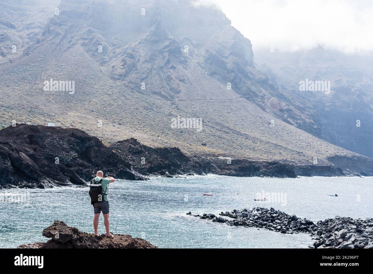 Fotograf am Rand einer Klippe vor dem Hintergrund des Ozeans und der Berge. Stockfoto