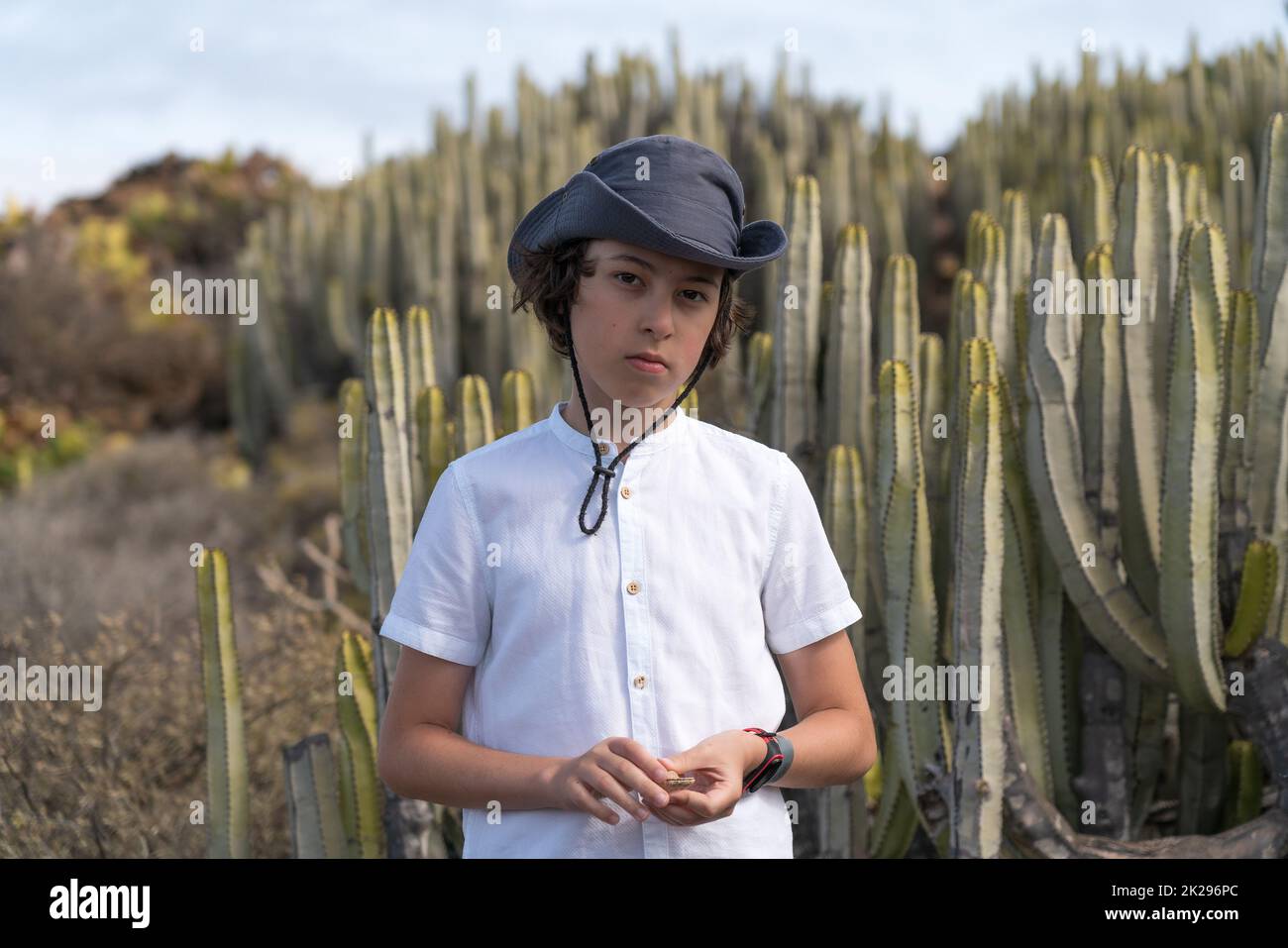 Porträt eines Teenagers in einem Poloshirt und einem Hut vor dem Hintergrund von Kakteen. Stockfoto