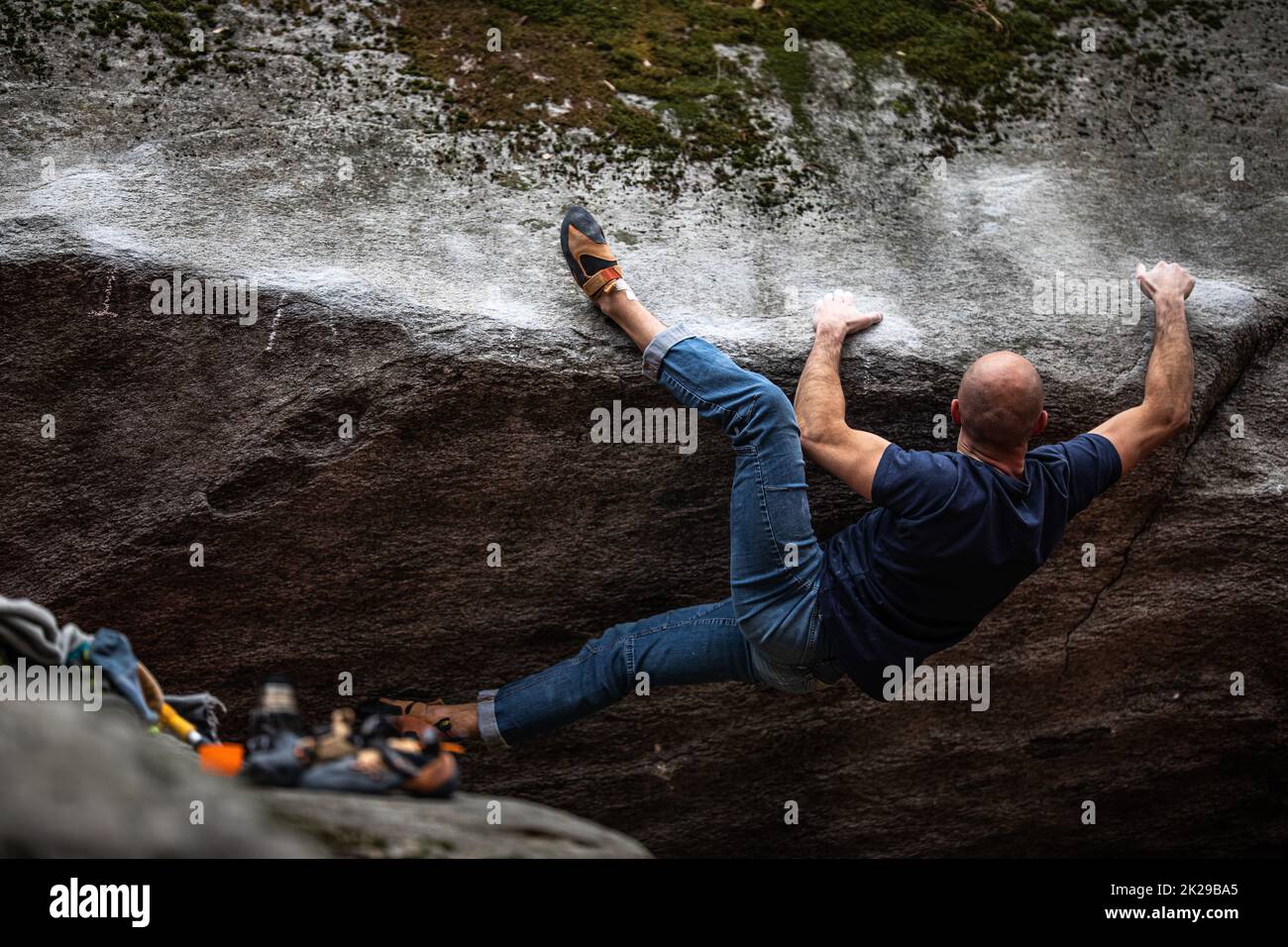 Ein Kletterer, der im Freien auf einem Felsbrocken klettert. Gruppe von Freunden, die sich im Freien mit Sport beschäftigen. Stockfoto