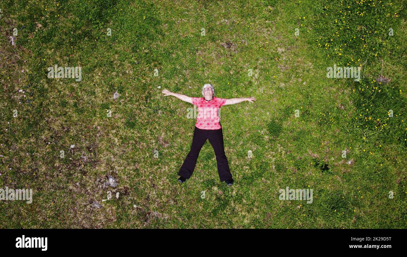 Drohnenaufnahme einer älteren Frau, die entspannt auf einer Bergwiese liegt Stockfoto