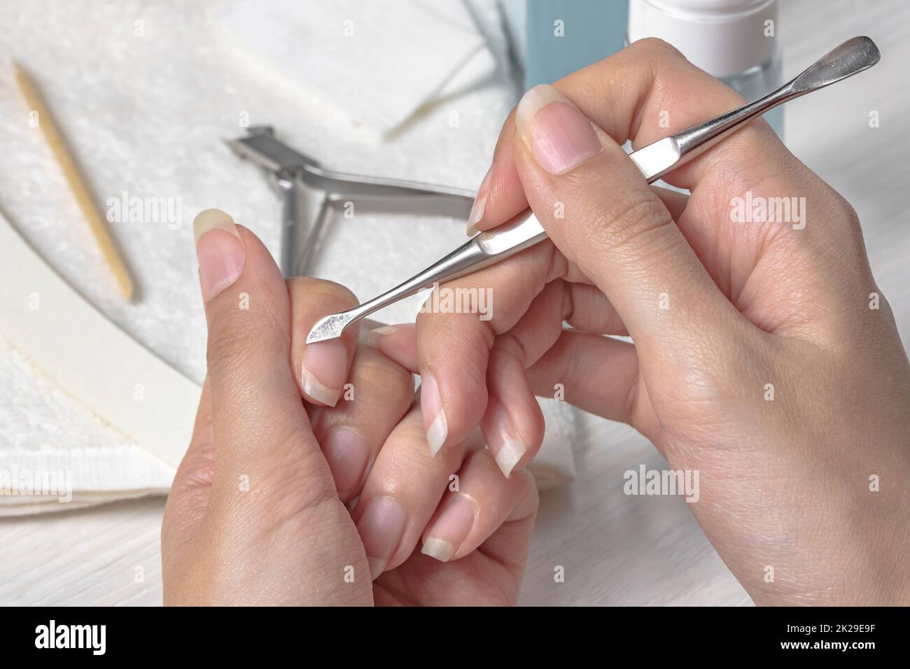 Maniküre. Die Nagelhaut mit einem Metalldrücker zurückschieben. Sich bei der Maniküre verletzen. Hautpflege, Hände, Nägel, Hygiene. Spa-Salon, Nagelsalon. Häusliche Pflege. Schönheit. Frauenhände Stockfoto