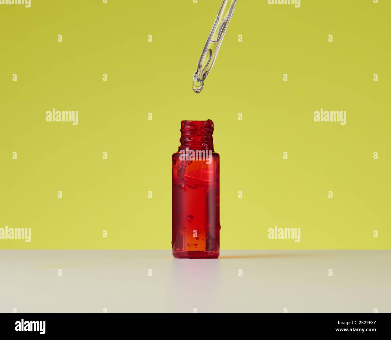 Ätherisches Öl, das aus dem Braunglas-Tropfer fällt. Rote Flasche Kosmetiköl mit einer Pipette Stockfoto