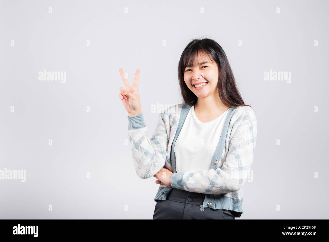 Eine Frau, die mit dem Finger zeigt, wie sie das V-Zeichen-Siegessymbol zeigt und in die Kamera schaut Stockfoto
