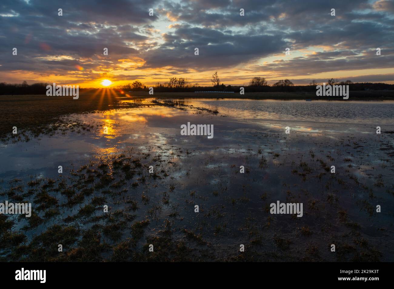 Überflutete Wiese nach Regen, Wolken und Sonnenuntergang Stockfoto