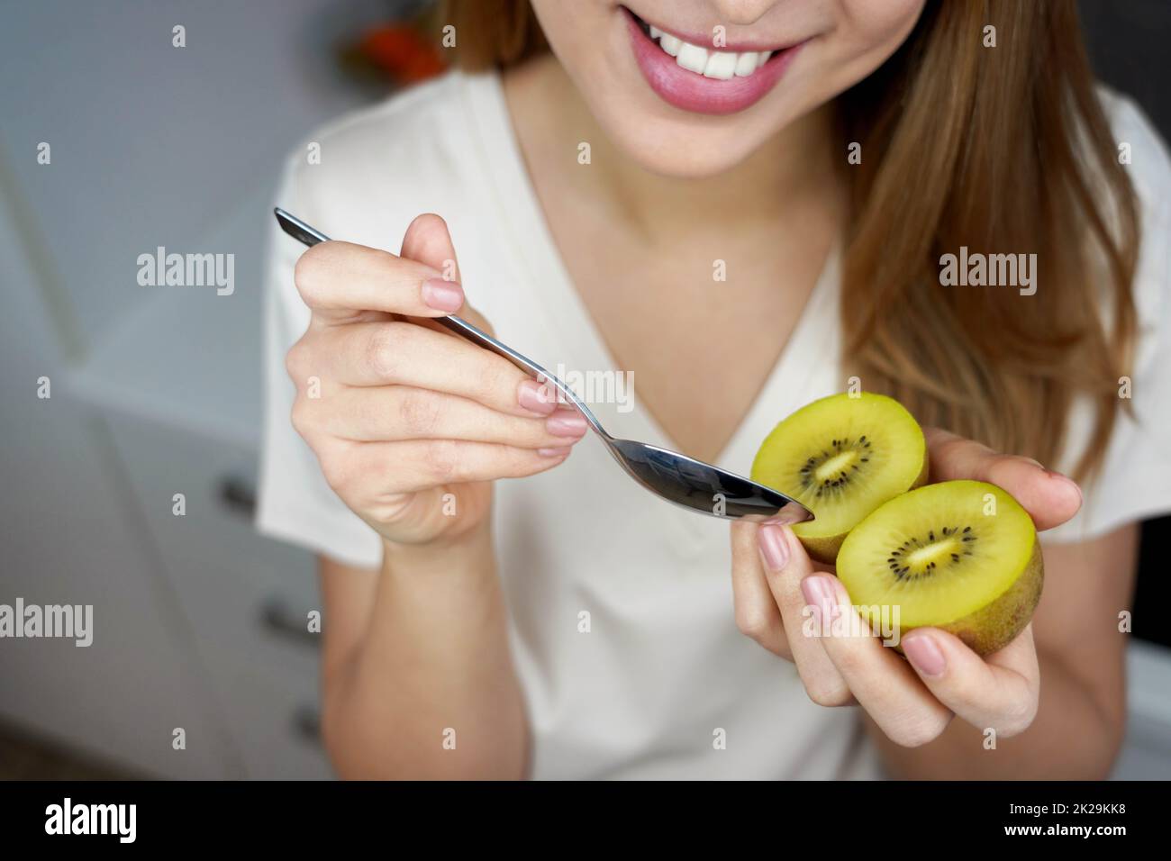 Glückliche junge, gesunde Frau, die zu Hause einen goldenen Kiwi isst. Antioxidans, Vitamin C, gesundes Konzept. Stockfoto