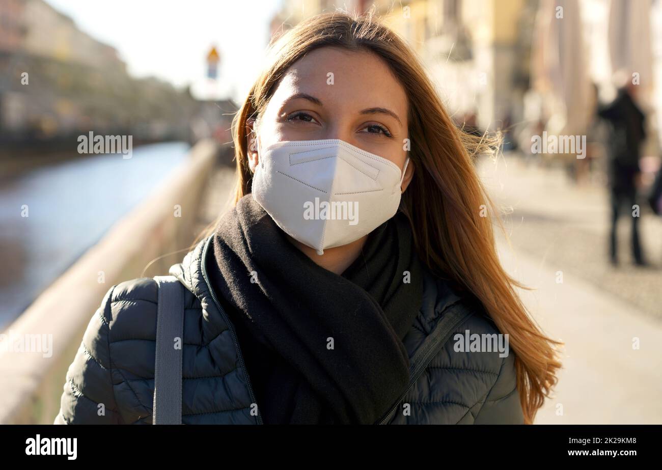 Hoffnungsvolle junge Frau, die eine Schutzmaske trägt und am Sonnenuntergang eines windigen Tages wegstarrt Stockfoto