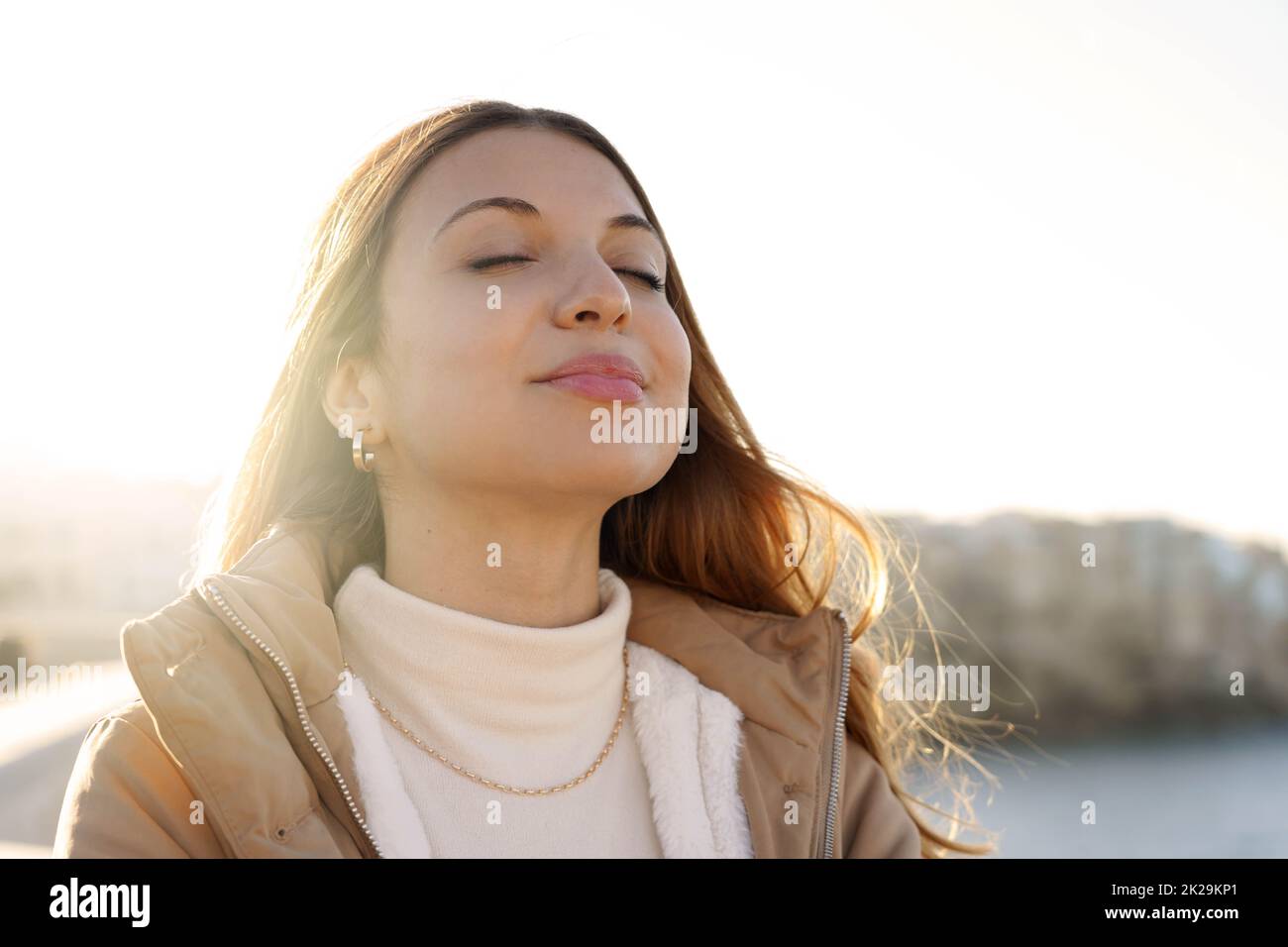 Junge charmante Frau atmet frische Luft und entspannt und lächelt bei Sonnenuntergang mit geschlossenen Augen Stockfoto