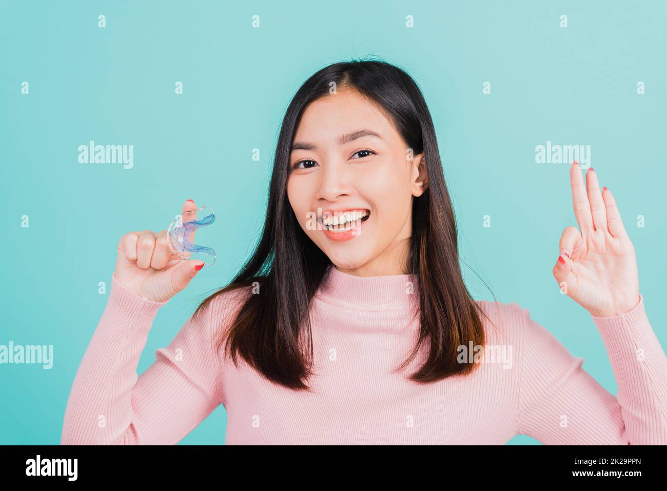Lächelnde Frau mit kieferorthopädischen Silikonhalterungen für die Zähne und Fingerklammern mit dem Zeichen OK Stockfoto