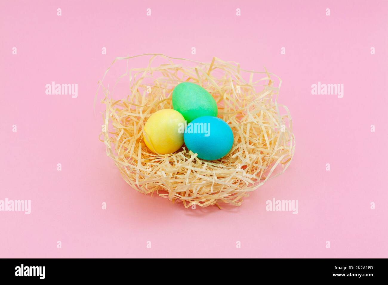 Ostereier in Pastelltönen in Heuernest mit pinkfarbenem Hintergrund. Stockfoto