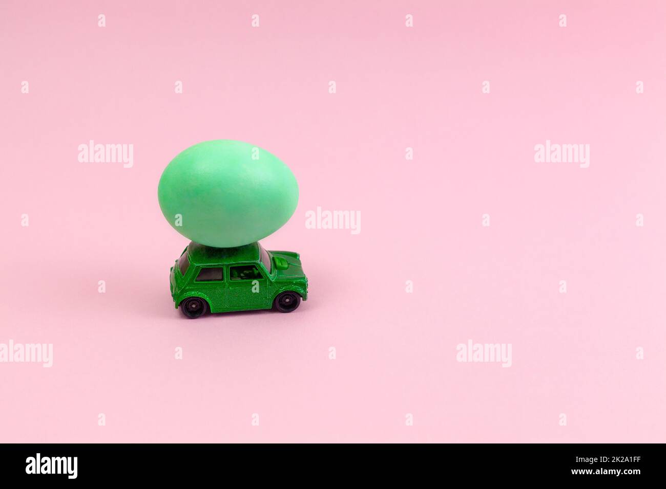 Ein grünes Spielzeugauto mit Osterei auf dem Dach. Osterkarte mit Platz für Text auf pinkfarbenem Hintergrund. Stockfoto