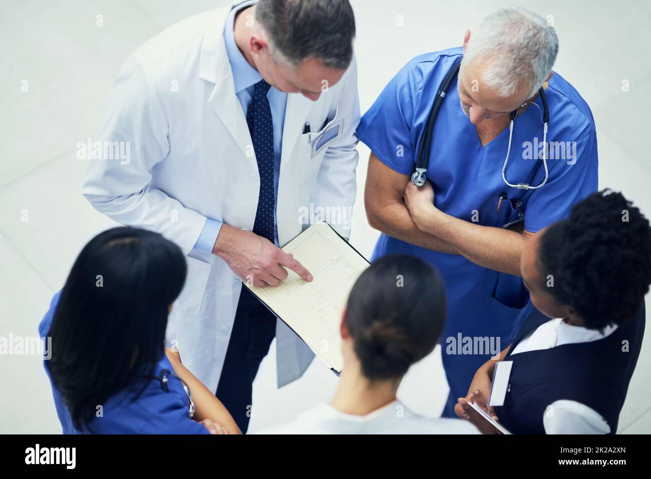 Diskutieren von Diagnosen. Aufnahme einer Gruppe von Ärzten, die sich über eine Krankenakte unterhalten, während sie in einem Krankenhaus stehen. Stockfoto