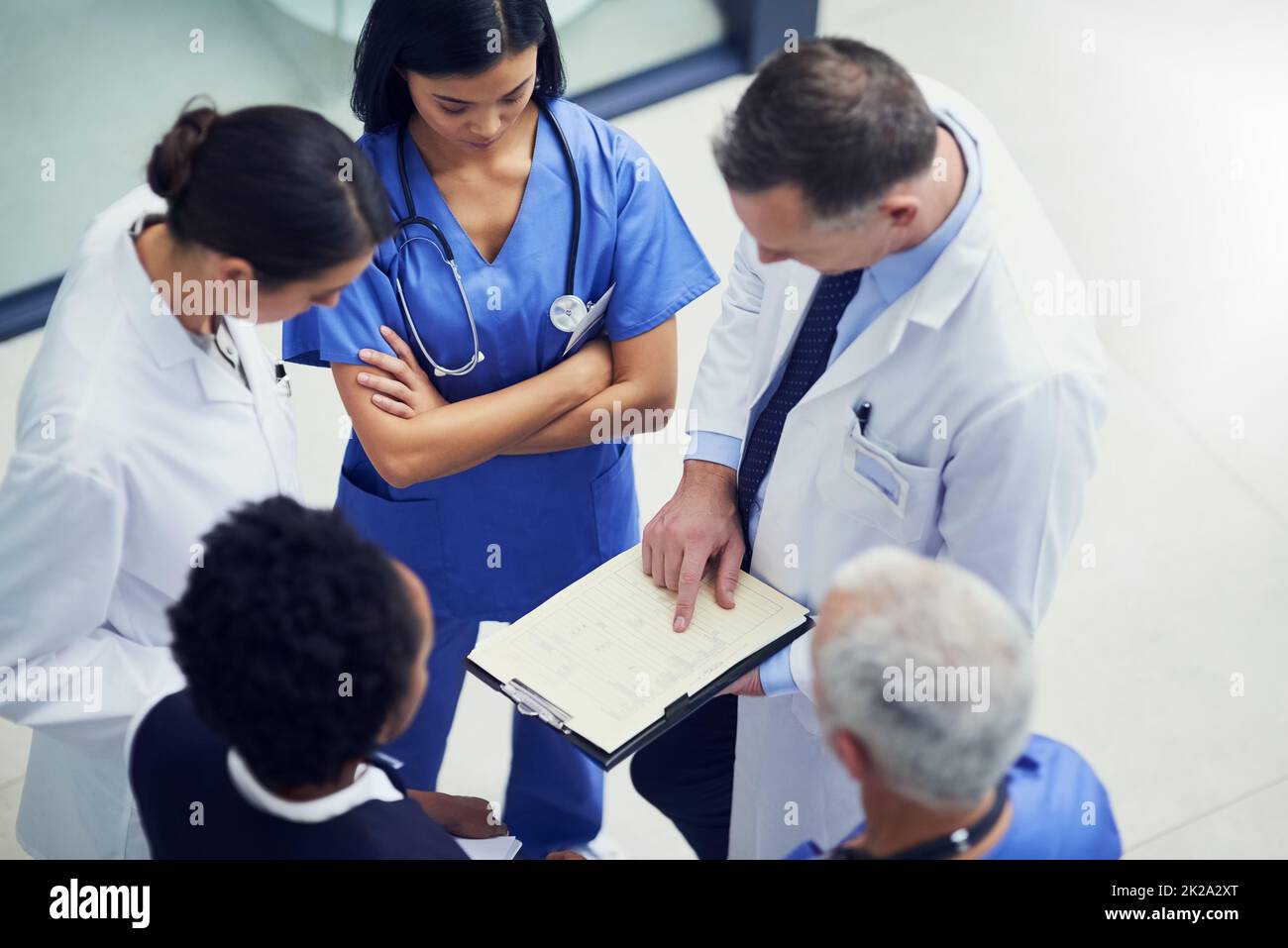 Gibt die Dosierung für diesen Patienten an. Aufnahme einer Gruppe von Ärzten, die sich über eine Krankenakte unterhalten, während sie in einem Krankenhaus stehen. Stockfoto