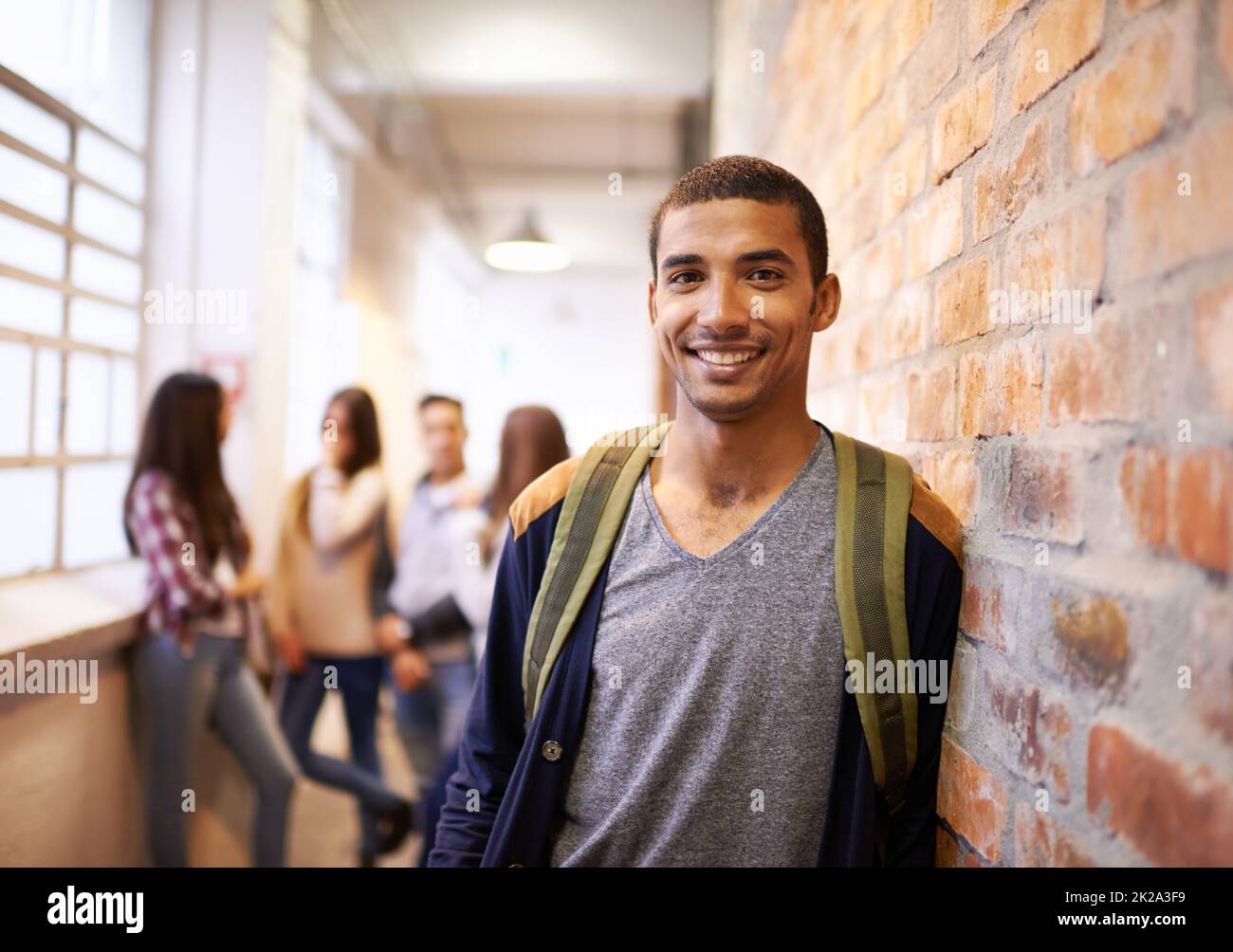 Freunde machen College-Spaß. Porträt eines hübschen jungen Studenten, der sich an einer Wand lehnte, mit seinen Freunden im Hintergrund. Stockfoto