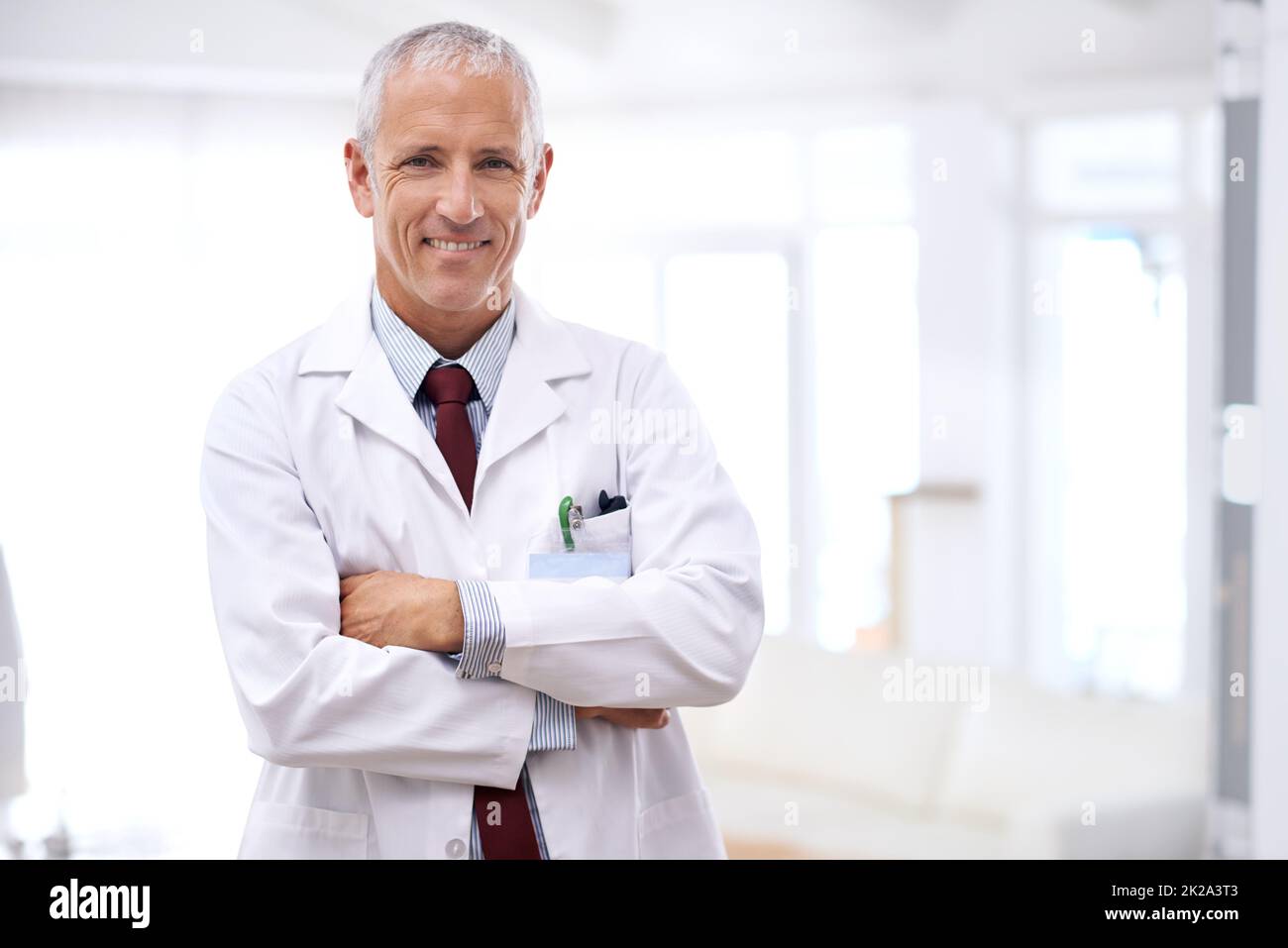 Ihre Gesundheit ist meine oberste Priorität. Porträt eines reifen Arztes, der mit gekreuzten Armen steht. Stockfoto