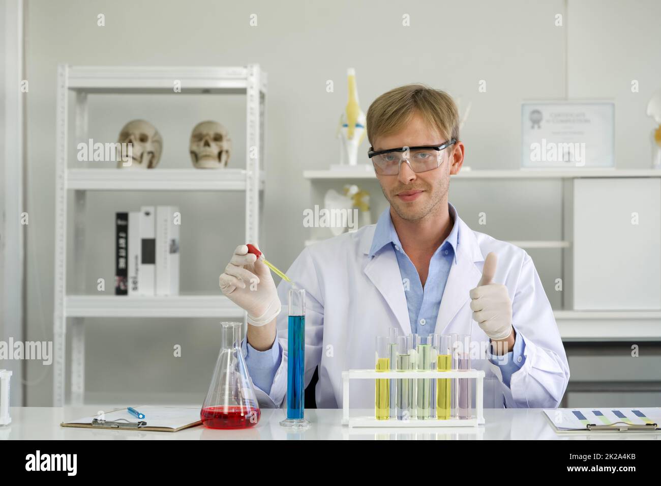 Ein junger brasilianischer Wissenschaftler mit Schutzbrillen mischt kosmetische Chemikalien sorgfältig zusammen. Arbeitsatmosphäre im chemischen Laboratorium. Mit Chemikalien gefüllte Reagenzgläser auf dem Tisch. Stockfoto