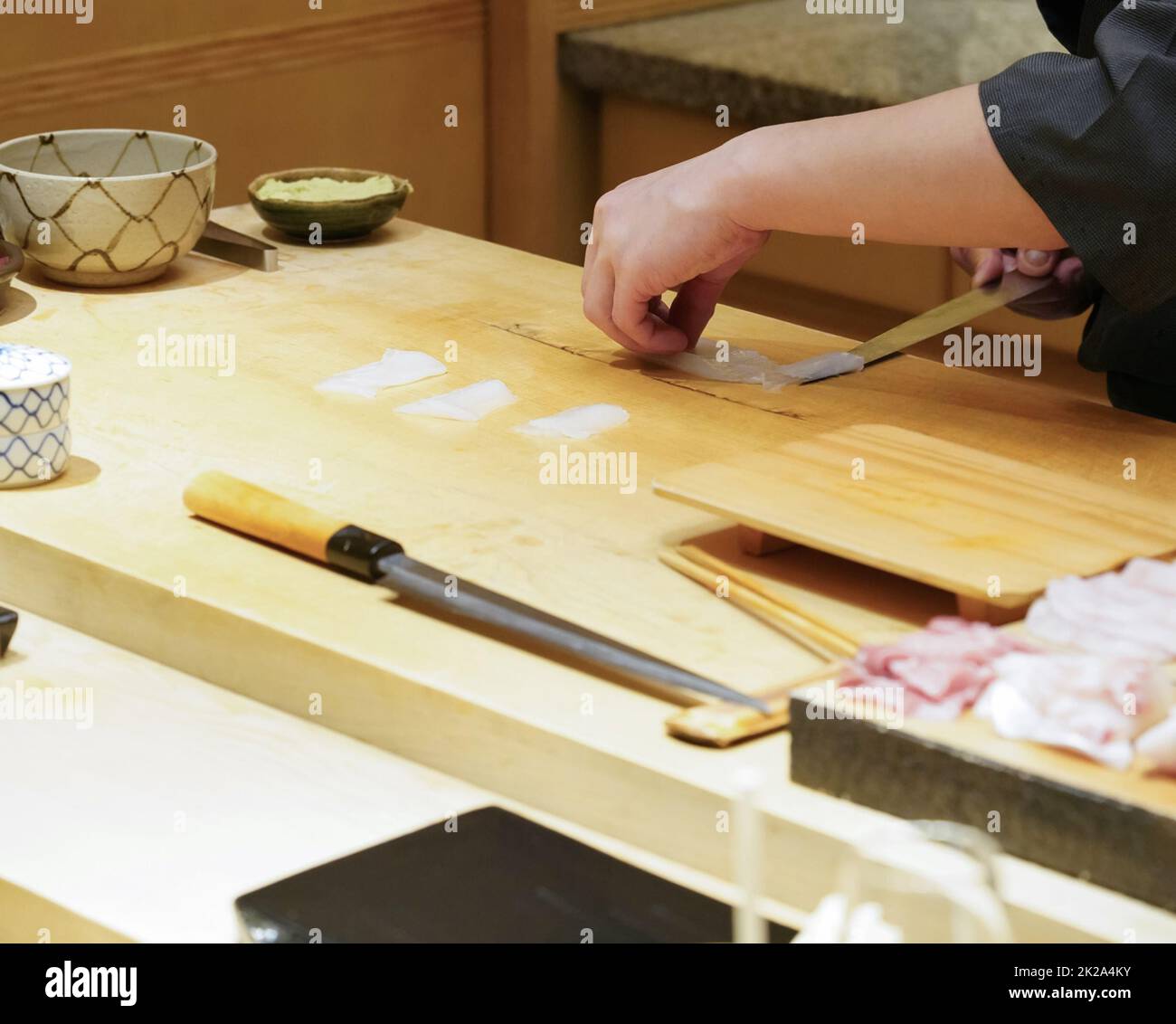 Der Koch verwendet scharfe Messer, um weiße Tintenfische für Sashimi zu schneiden. Stockfoto