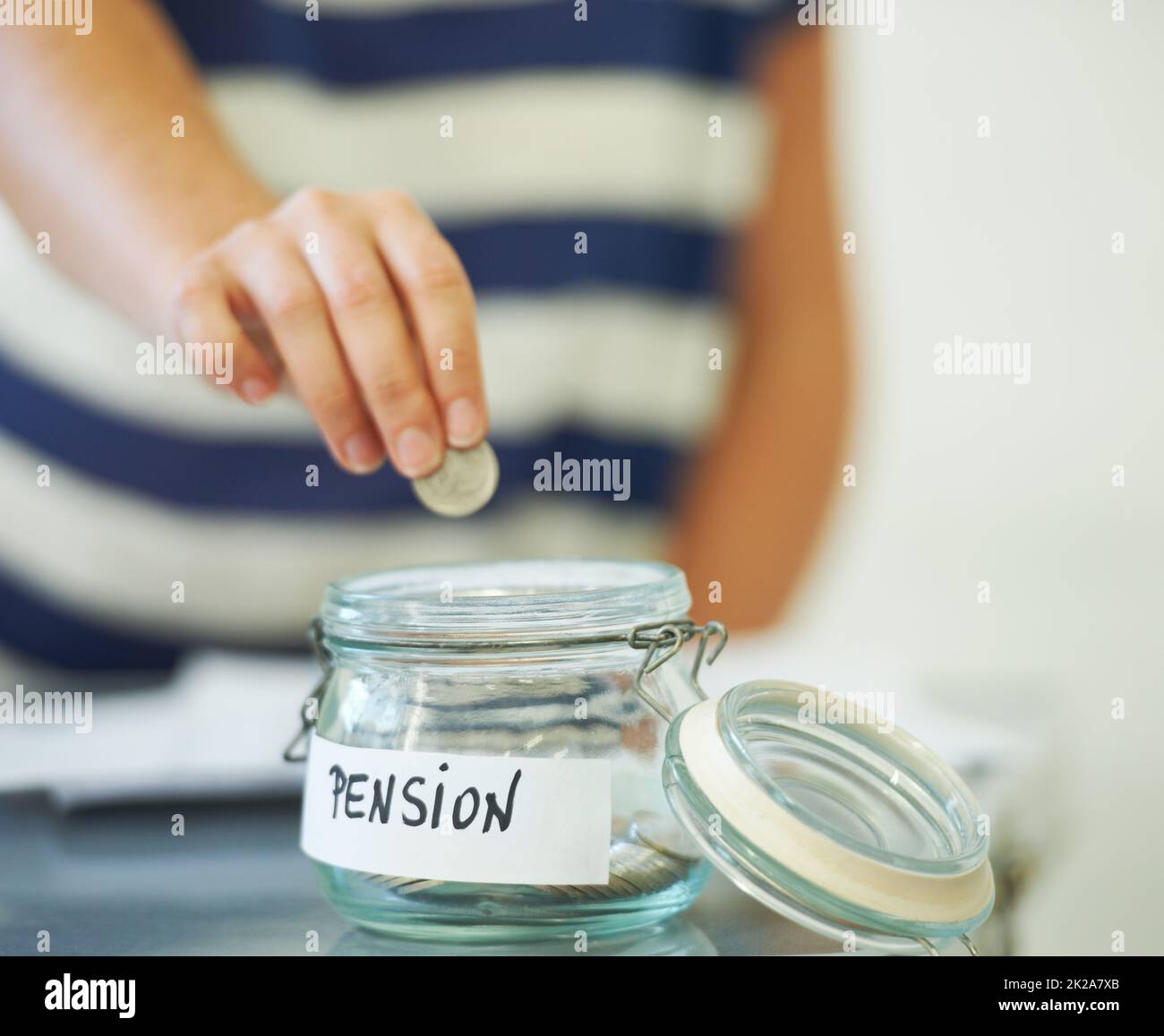 Sparen Sie Geld für Geld. Eine Person, die einen Penny in ein Glas mit der Aufschrift amp039Pensionamp039 legt. Stockfoto