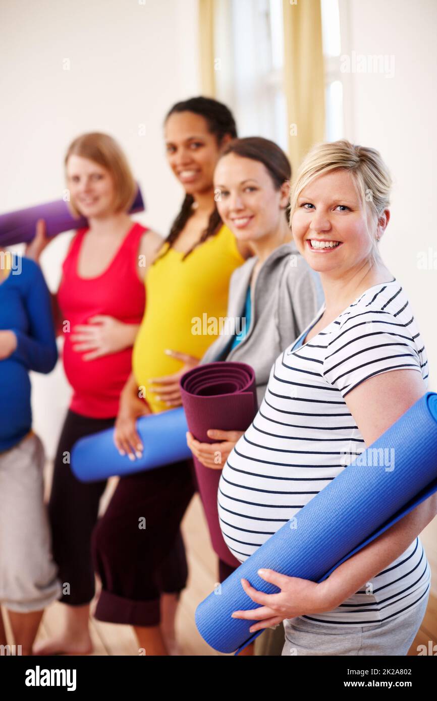 Während der Schwangerschaft aktiv bleiben. Eine multiethnische Gruppe von Schwangeren, die ihre Trainingsmatten in einem Fitnessstudio halten. Stockfoto