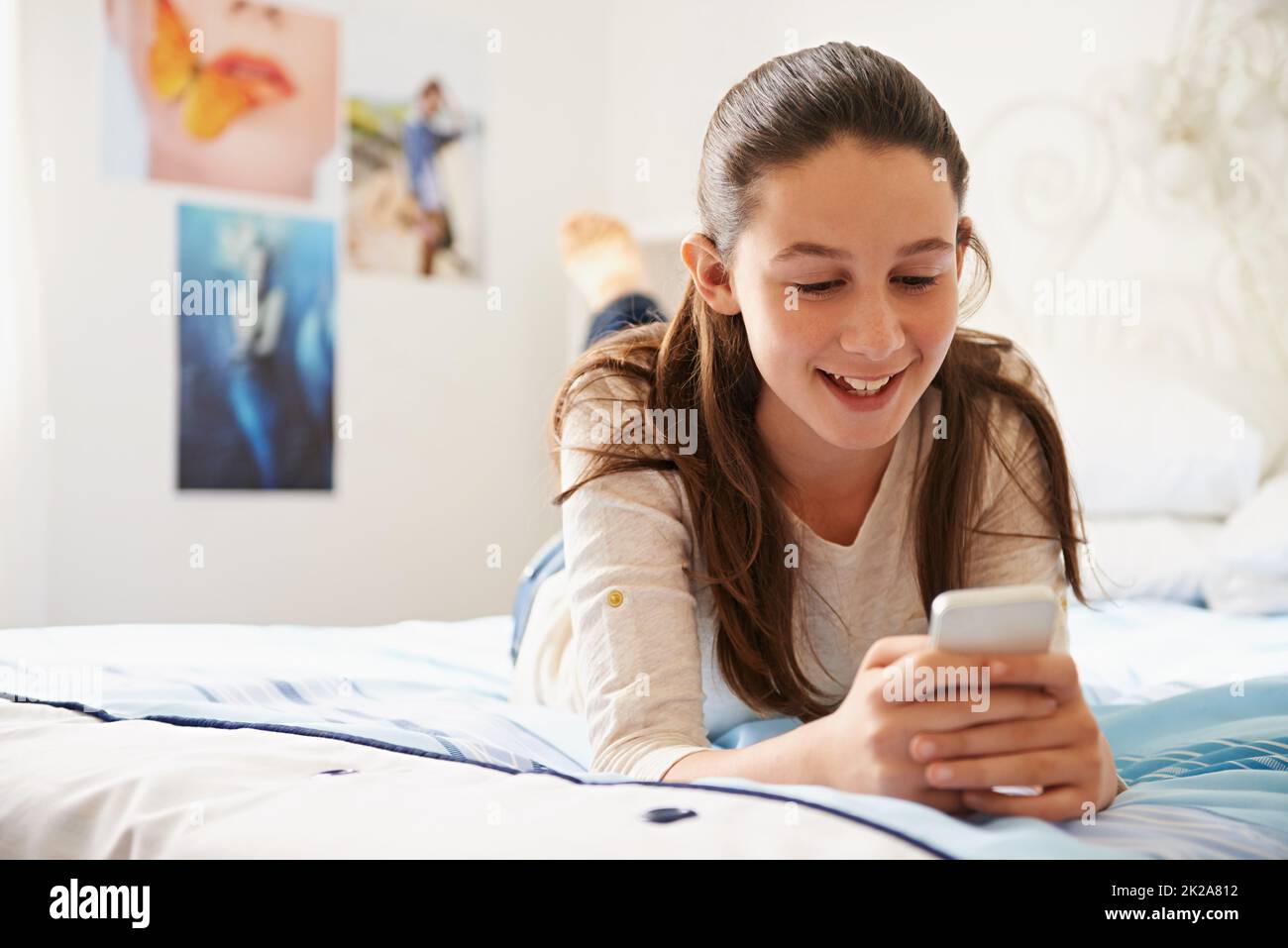 Planen Sie etwas großes. Aufnahme eines Teenagers, das auf ihrem Bett liegt und auf ihrem Telefon SMS schreibt. Stockfoto