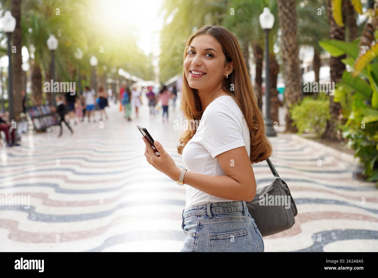 Frühling Mädchen zu Fuß drehen sich um halten Smartphone in der Stadt Stockfoto