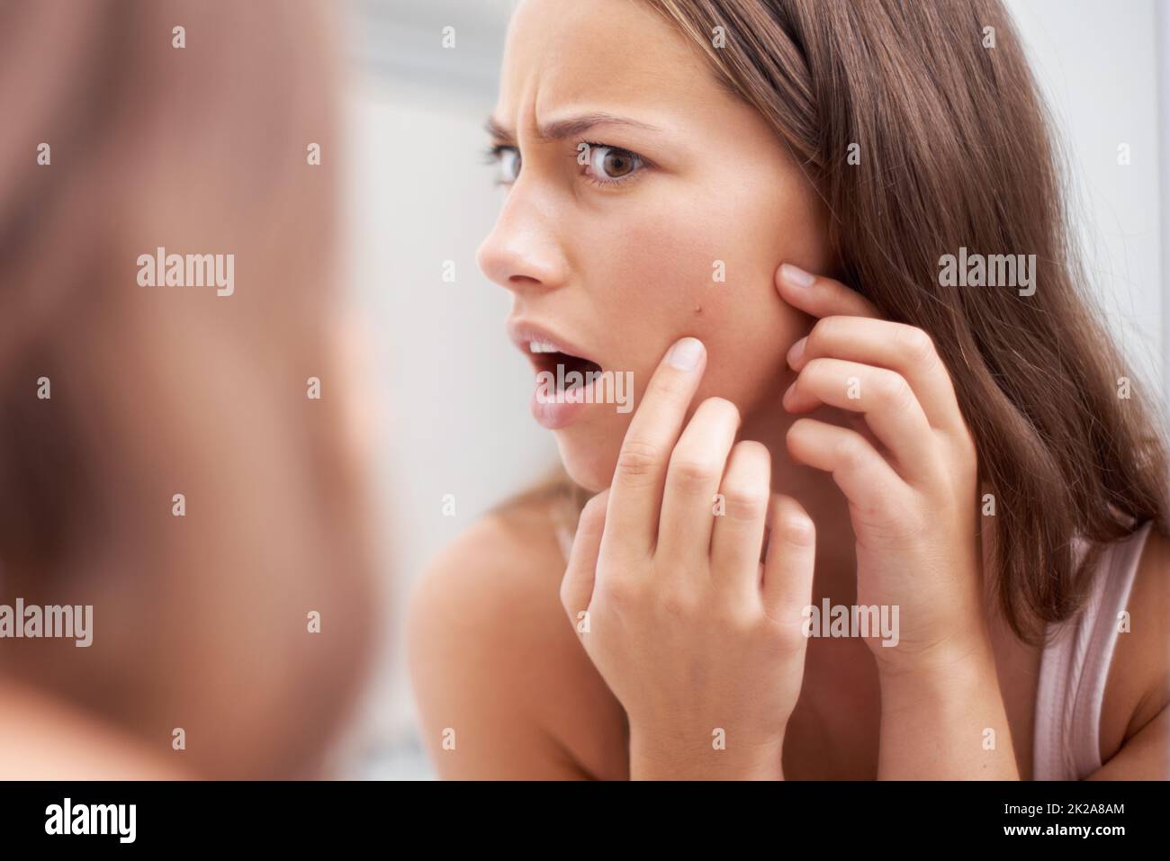 Was Für Ein Pickel. Eine junge Frau, die schockiert aussieht, als sie ihre Haut untersucht. Stockfoto