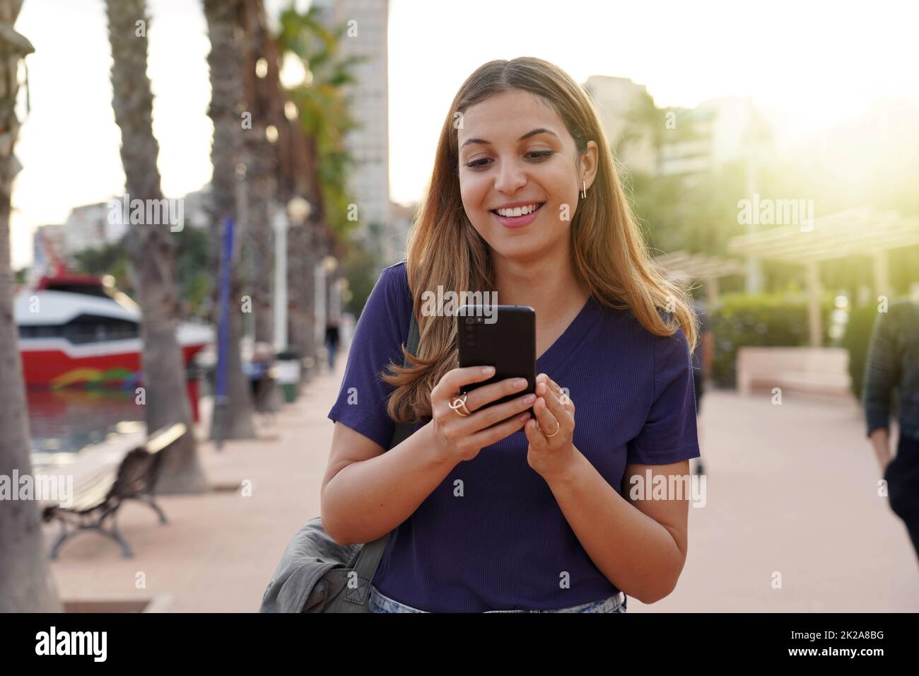 Attraktive junge Frau, die ihr Smartphone auf der Stadtpromenade beobachtete Stockfoto