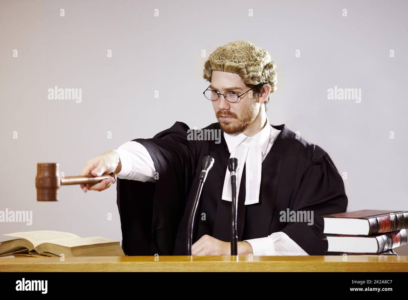 Stille. Seriöse junge Richterin sitzt im Gerichtssaal mit strengem Gesichtsausdruck, während sie einen Gavel aushält. Stockfoto