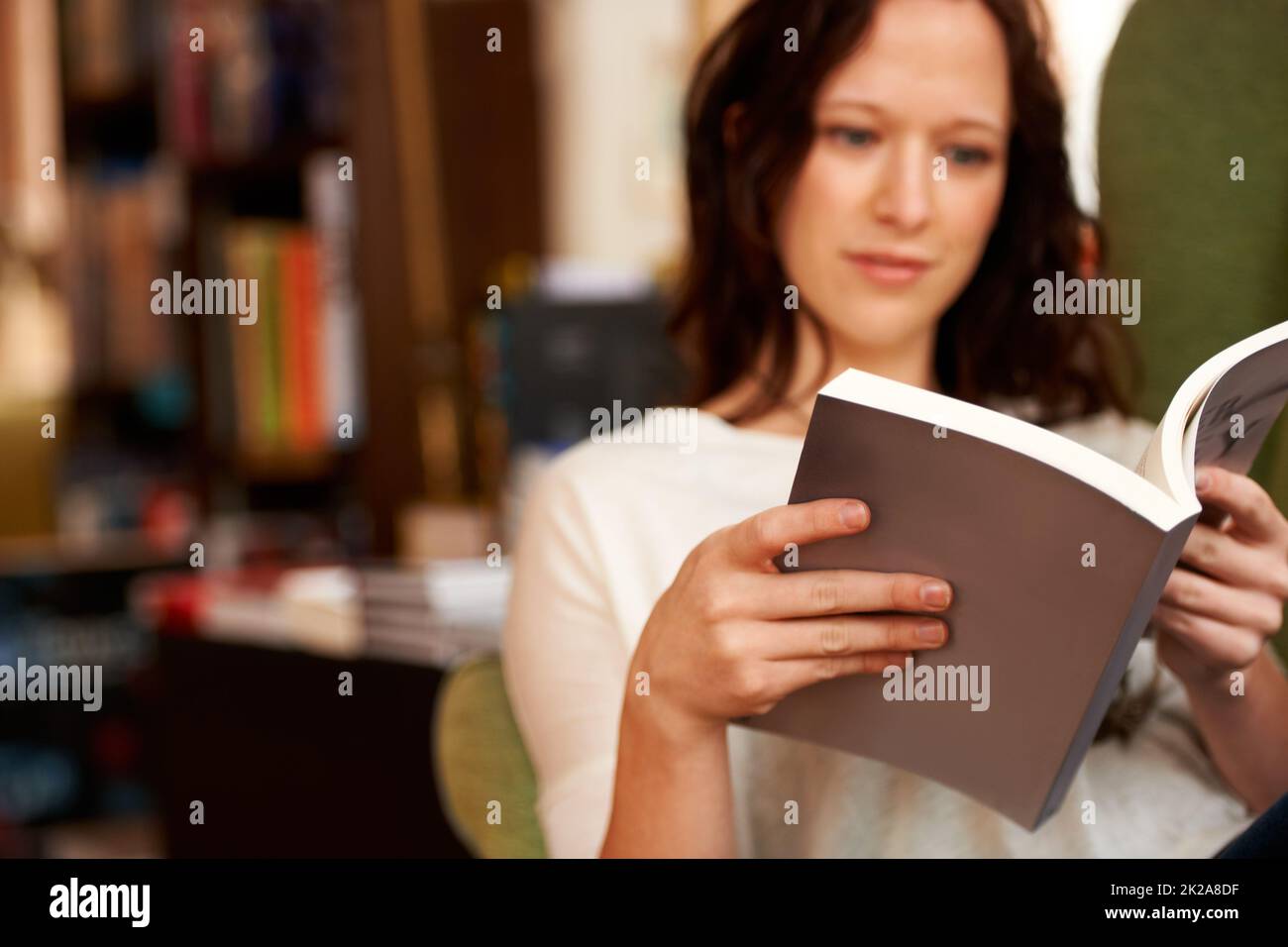 Eingetaucht in die Worte. Eine junge Frau liest ruhig ein Buch, während sie auf einem Stuhl sitzt. Stockfoto