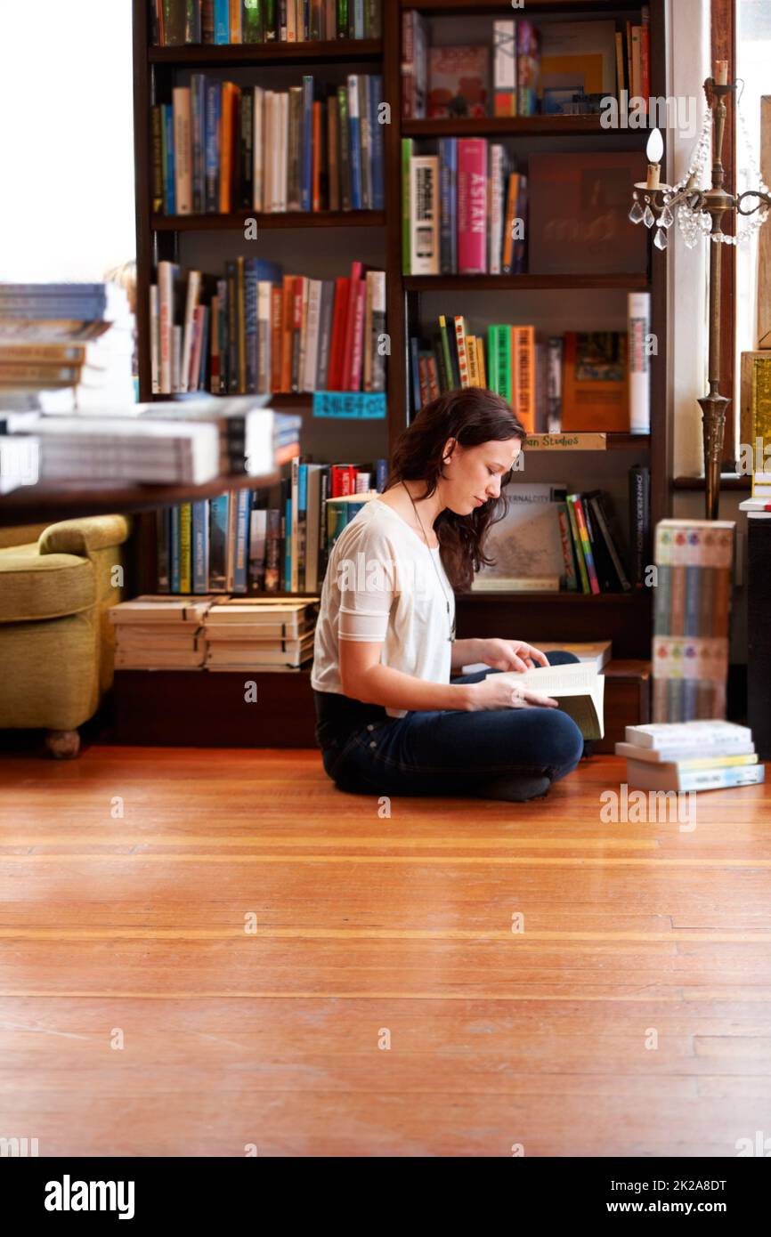 Sie hat Zeit zum Lesen. Eine junge Frau, die mit gekreuzten Beinen auf dem Boden sitzt und liest. Stockfoto