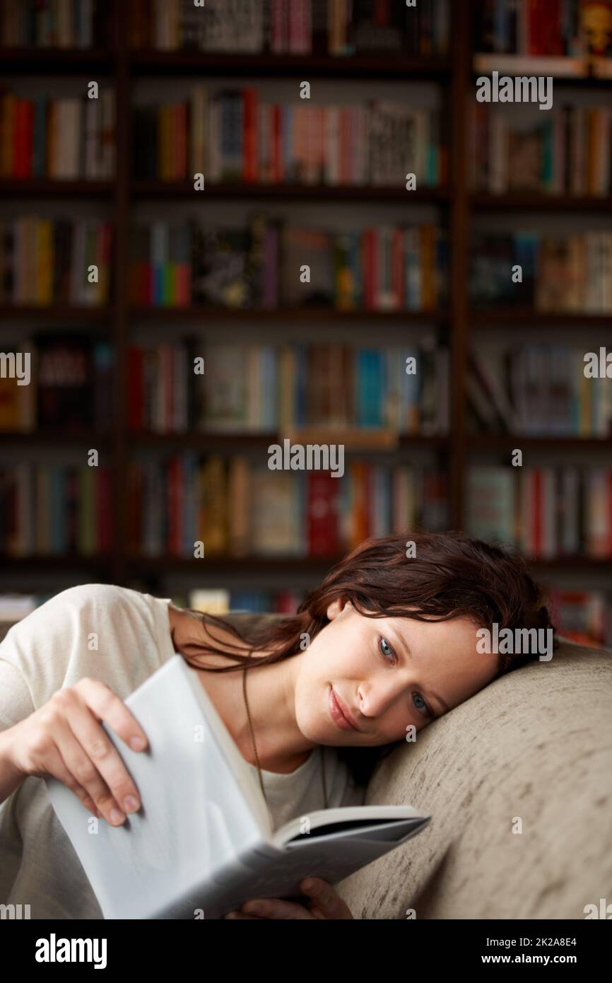 In ihrer eigenen Welt. Eine attraktive junge Frau, die sich auf einem Sofa mit einem Buch - Kopierraum entspannt. Stockfoto