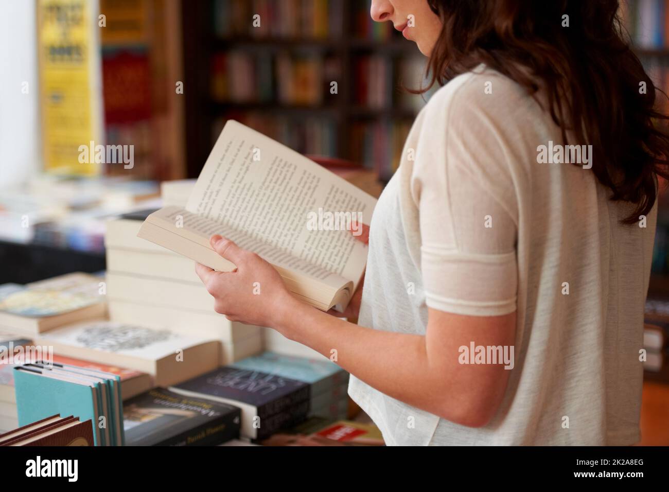 Verloren in den Seiten. Eine ausgeschnittene Aufnahme einer jungen Frau, die ein Buch liest, während sie in einer Buchhandlung steht. Stockfoto