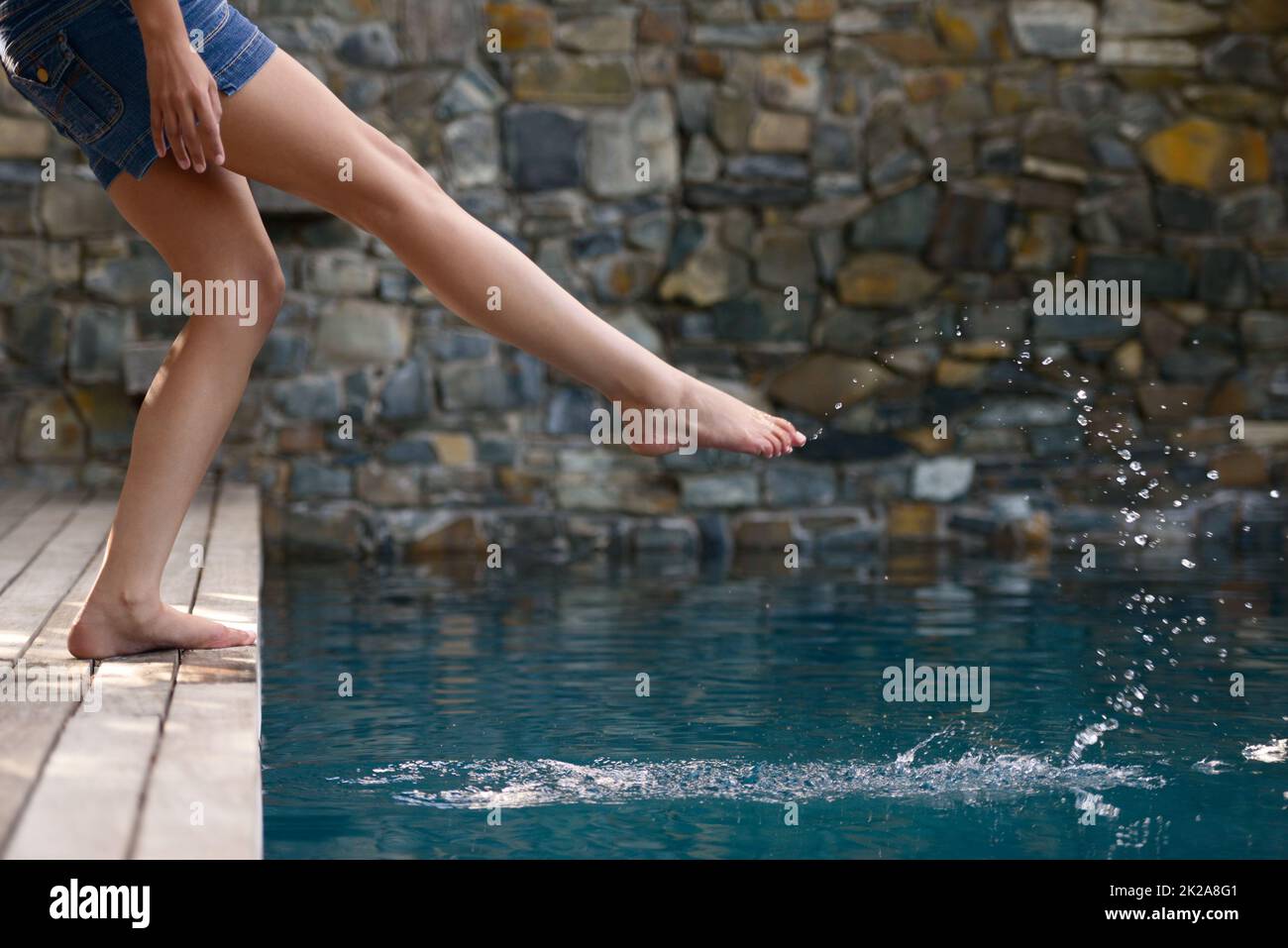 Einfach nur herumplanschen. Ein kurzer Schuss einer jungen Frau, die das Wasser eines Schwimmbades testet. Stockfoto