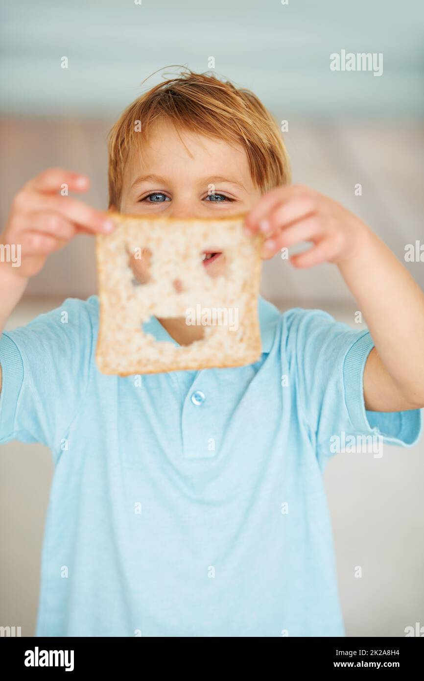 Das Essen macht mich glücklich. Aufnahme eines kleinen Jungen, der eine Scheibe Brot mit einem ausgeschnittenen Smiley-Gesicht hochhält. Stockfoto