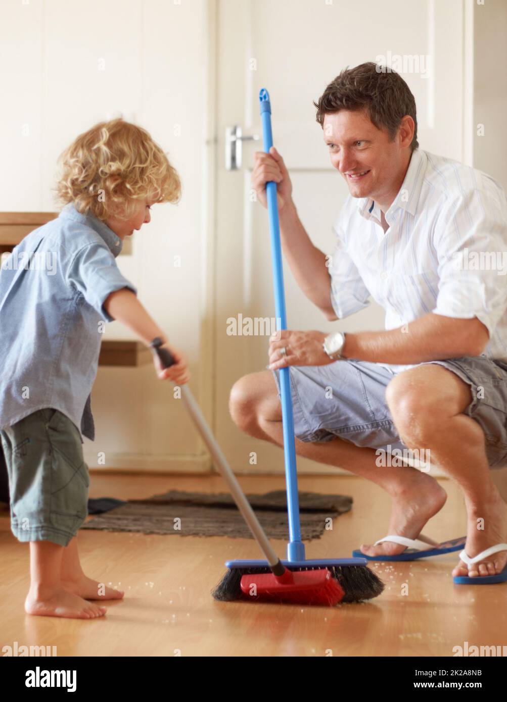 Sauber halten. Ein Vater und ein Kleinkindsohn fegen in ihrem Haus Sand zusammen. Stockfoto