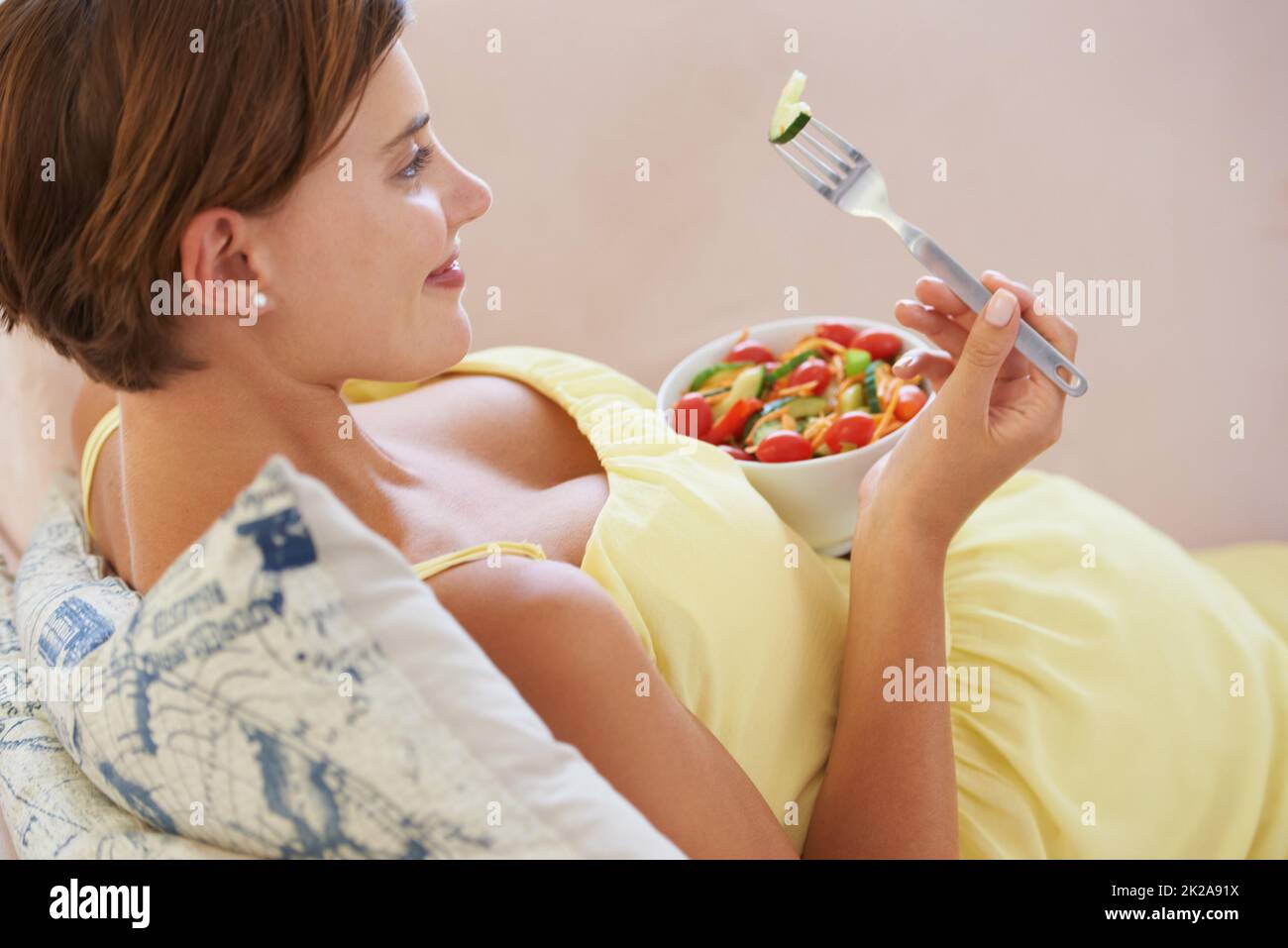 Lecker. Eine junge Schwangere genießt einen gesunden Salat, während sie sich auf der Couch entspannt. Stockfoto