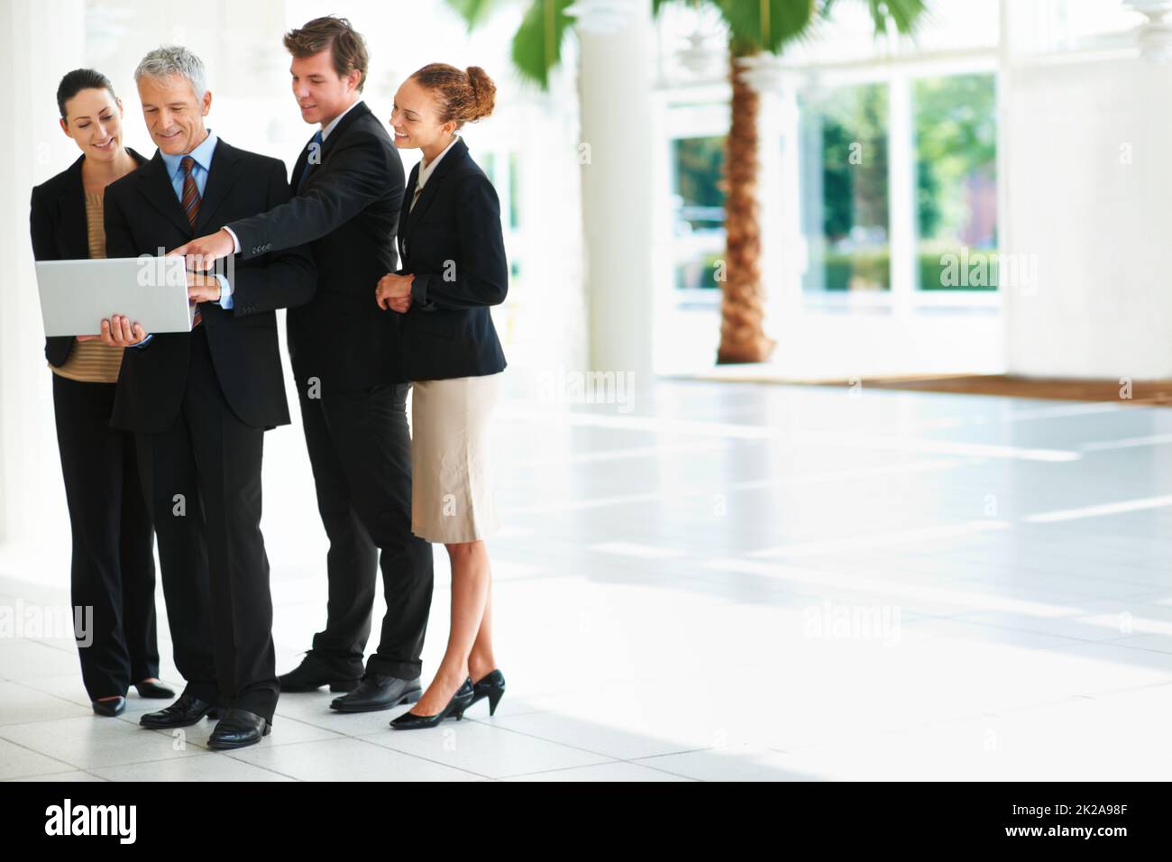Geschäftsabläufe ermöglichen. Aufnahme einer Gruppe von Geschäftsleuten, die über einen Laptop reden, während sie in einer Bürolobby stehen. Stockfoto