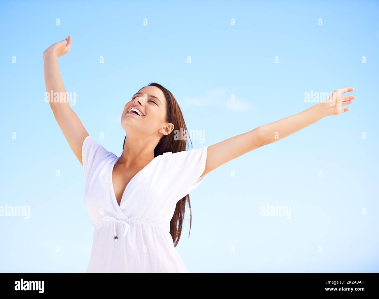 Freiheit gegen einen blauen Himmel. Eine unbeschwerte junge Frau, die mit ausgestreckten Armen vor einem blauen Himmel steht. Stockfoto