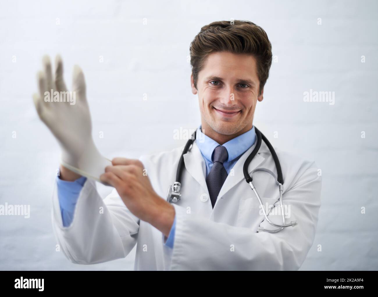 Das wird nicht lange dauern Aufnahme eines lächelnden Arztes, der an einem chirurgischen Handschuh zieht. Stockfoto