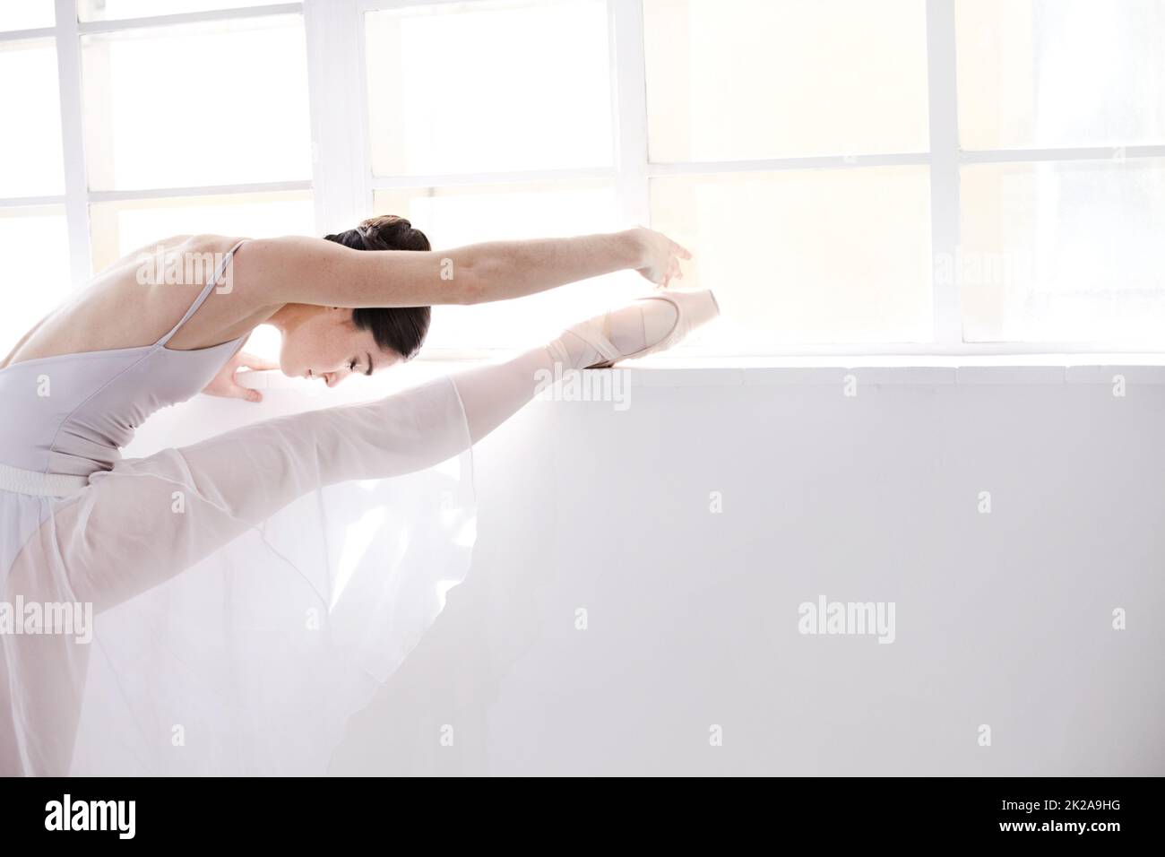 Anmut in Bewegung. Geschmeidige junge Ballerina, die sich entlang einer weißen Wand erstreckt. Stockfoto