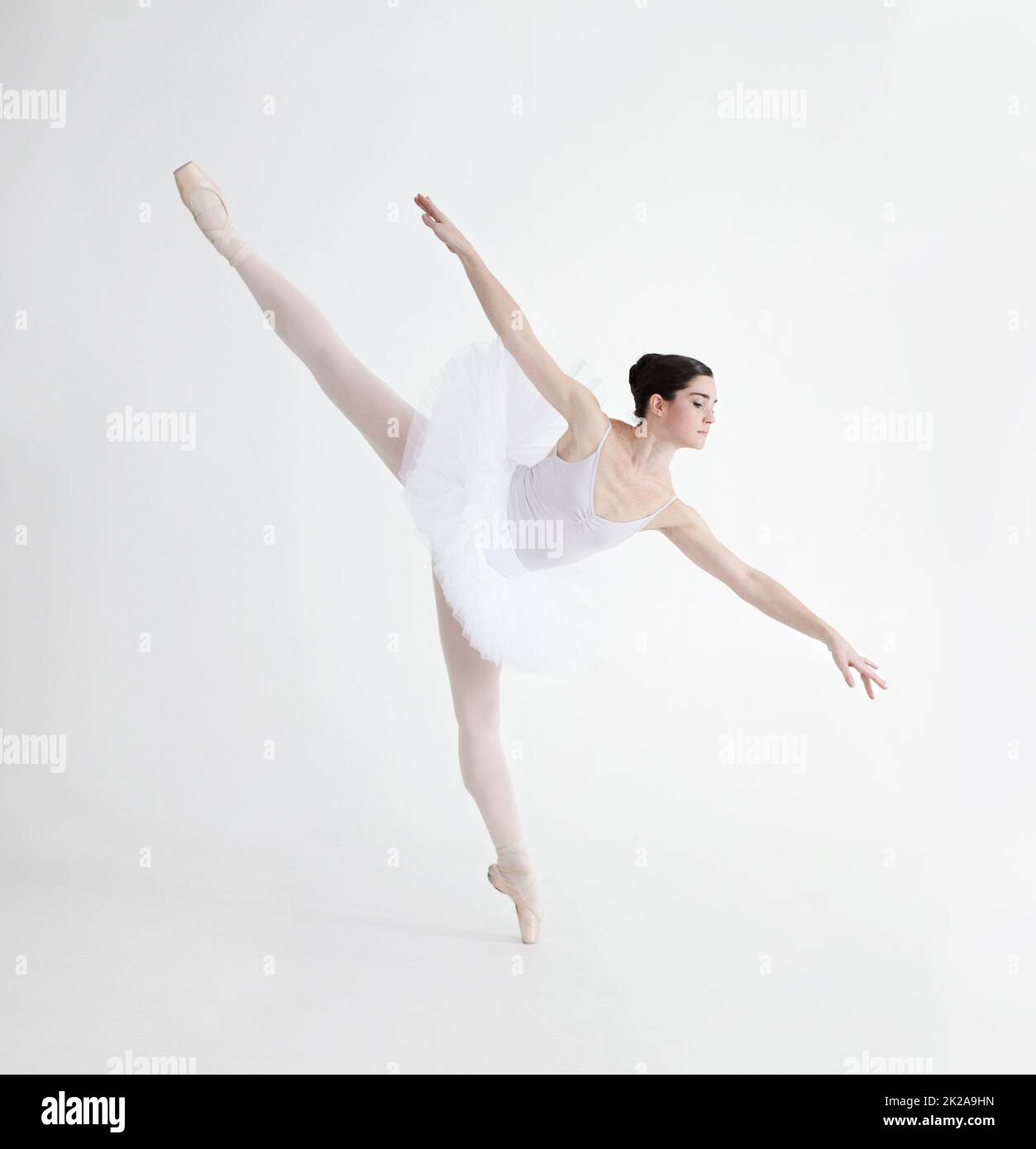 Ausgewogenheit ist entscheidend. Elegante junge Ballerina tanzt en pointe auf weißem Hintergrund in Penche-Position. Stockfoto