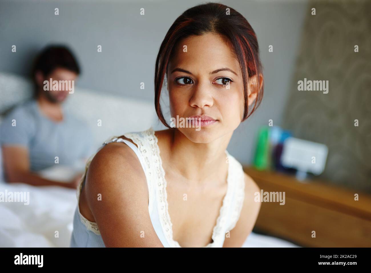 Beziehungsprobleme. Aufnahme einer verärgerten Frau, die auf der Seite ihres Bettes mit ihrem Freund im Hintergrund sitzt. Stockfoto