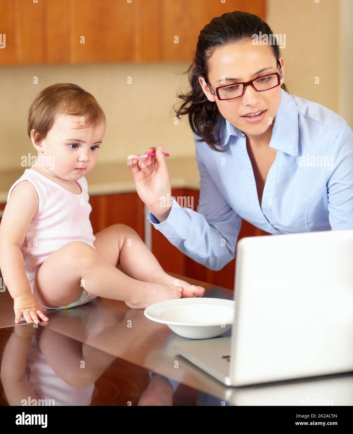 Eine zusätzliche Hand wäre nützlich. Aufnahme einer alleinerziehenden Mutter, die ihr Baby füttert, während sie versucht, an ihrem Laptop zu arbeiten. Stockfoto