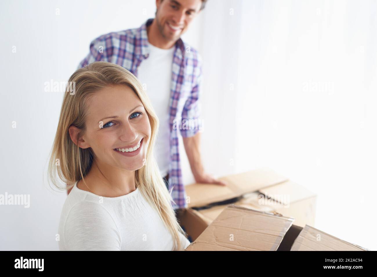 Glücklich, ein eigenes Zuhause zu haben. Eine lächelnde Frau, die einen braunen Pappkarton trägt, während ihr Freund aufschaut. Stockfoto