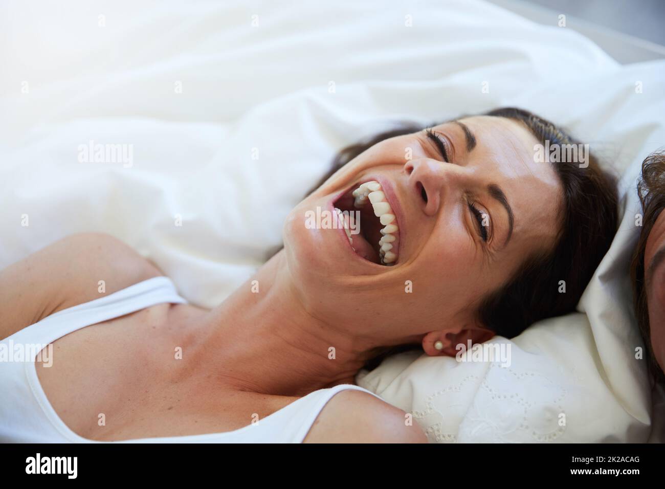 Nichts Besseres als Lachen, um die Stimmung zu heben. Aufnahme einer lachenden Frau, die sich im Bett neben ihrem Mann entspannt. Stockfoto