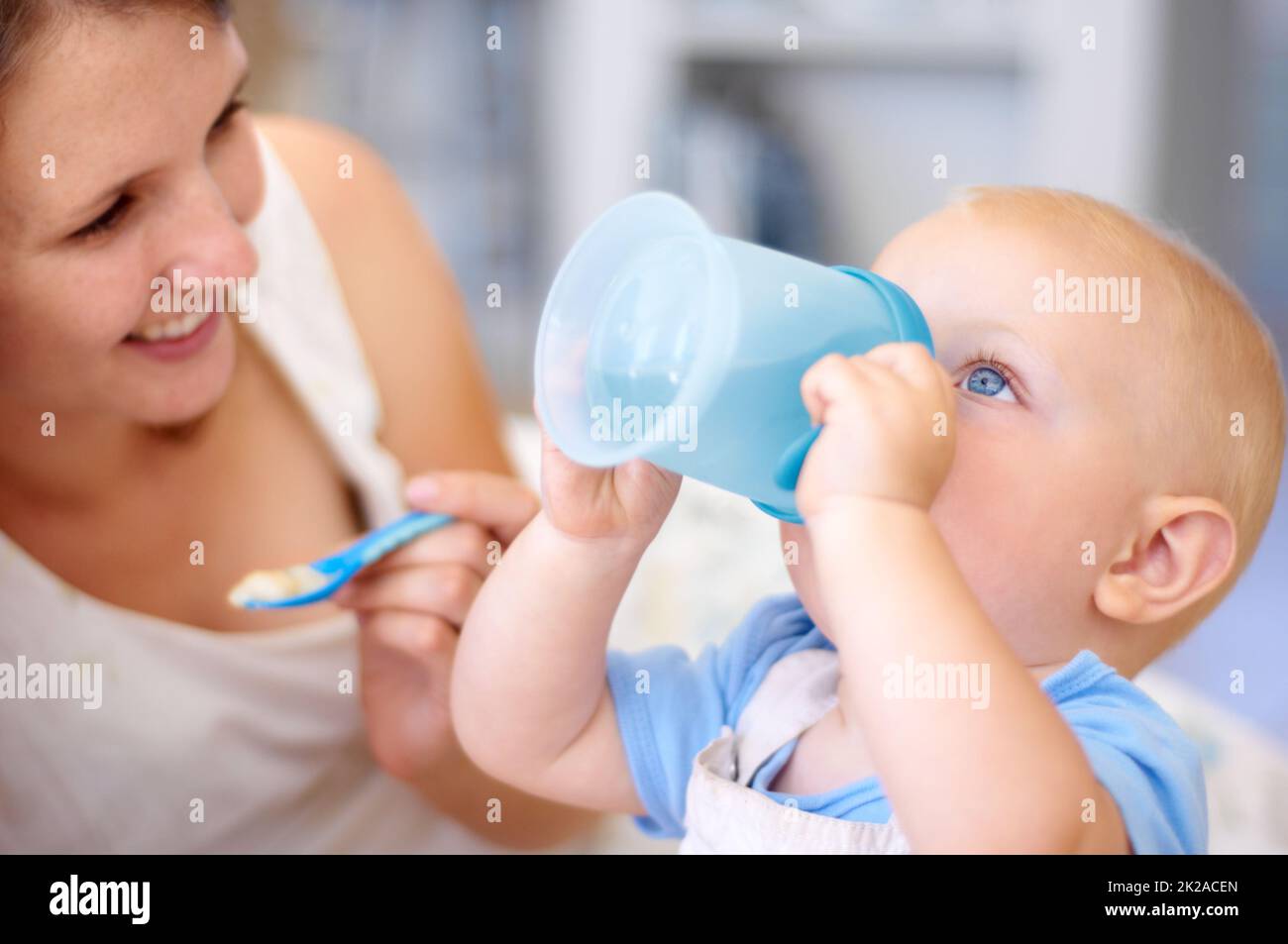 Trinkt ganz allein. Eine junge Mutter beobachtet, wie ihr kleiner Junge aus seinem sippy Cup trinkt. Stockfoto