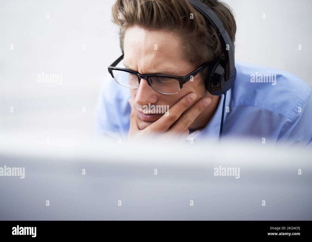 In seine Arbeit aufgenommen. Ein hübscher junger Geschäftsmann, der ein Headset trägt, während er sich auf seinen Computerbildschirm konzentriert. Stockfoto