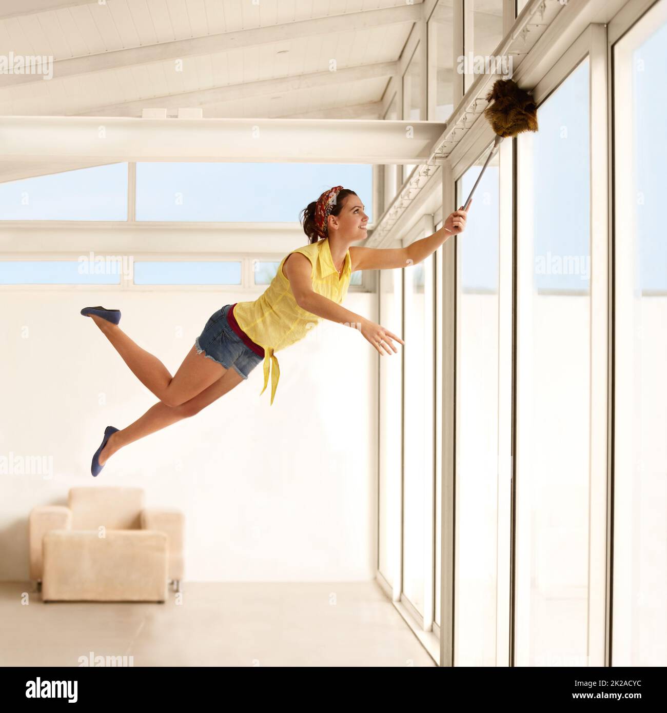 Shes eine Hausarbeit Fee. Junge Frau, die durch die Luft schwebt, während sie ihr Haus staubt. Stockfoto