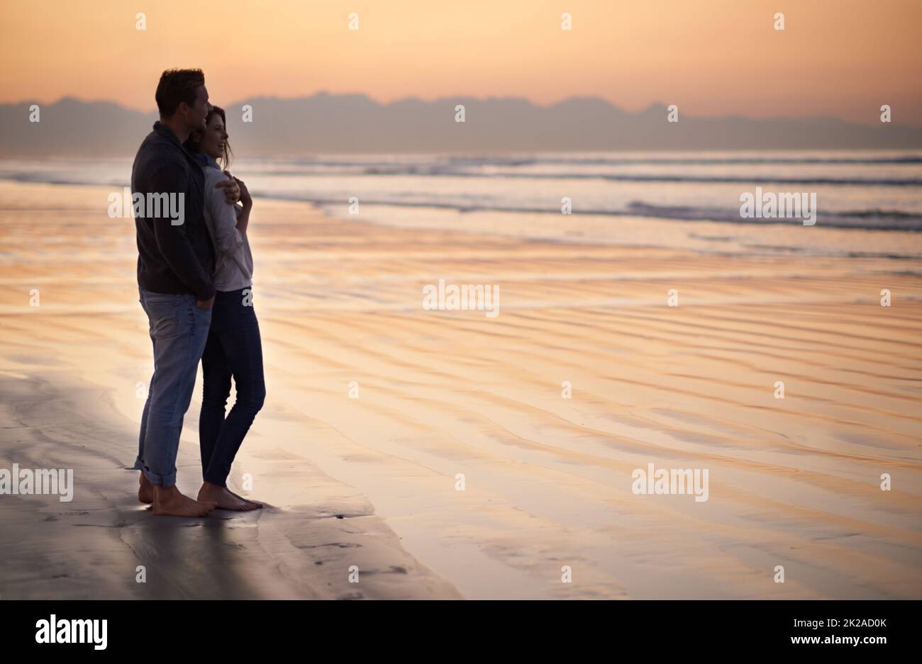 Es gibt nichts wie junge Liebe. Silhouette eines jungen Paares, das einen romantischen Spaziergang am Strand genießt. Stockfoto