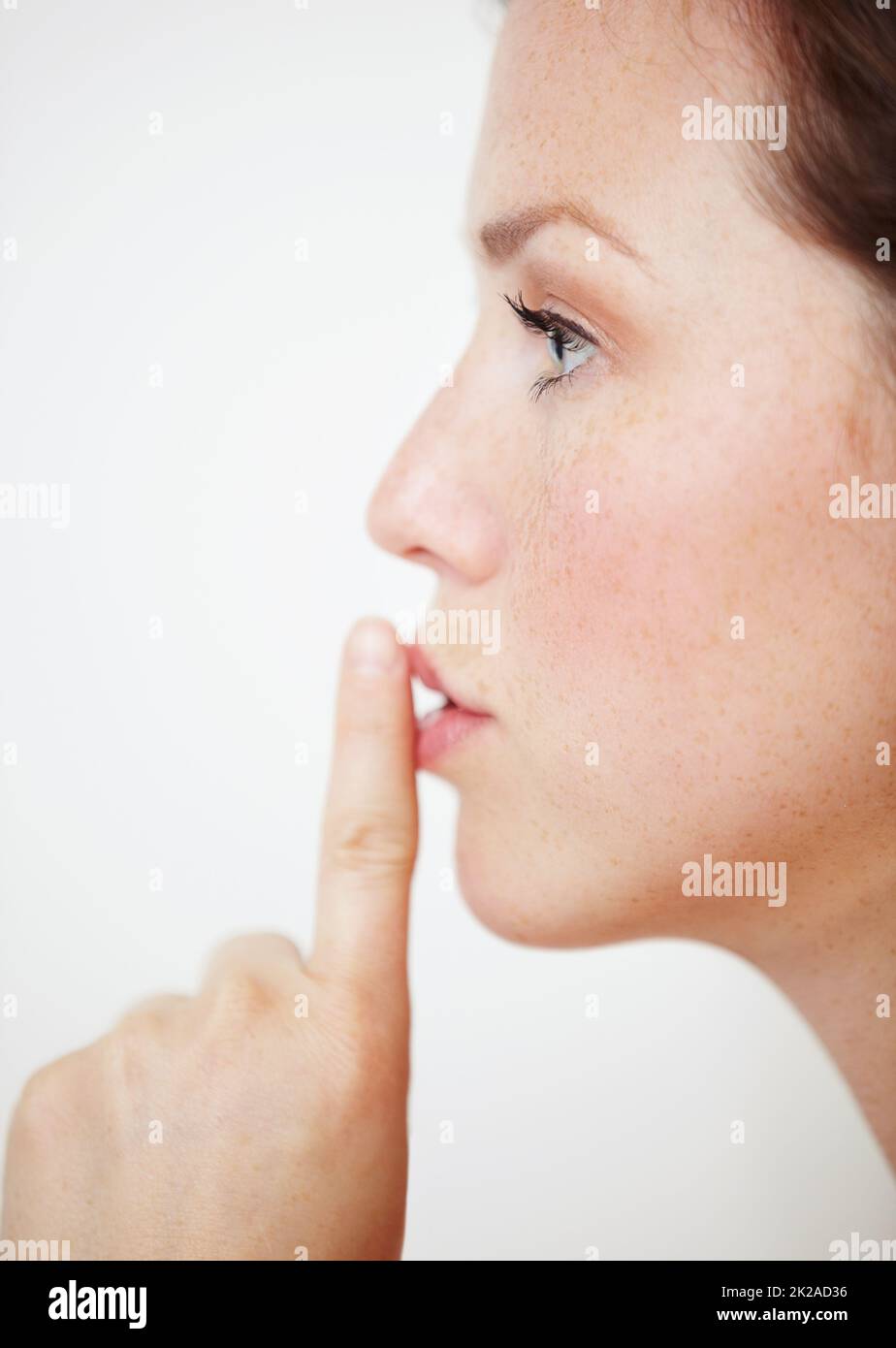 Kein Wort. Profil einer schönen jungen Frau mit dem Finger auf den Lippen. Stockfoto