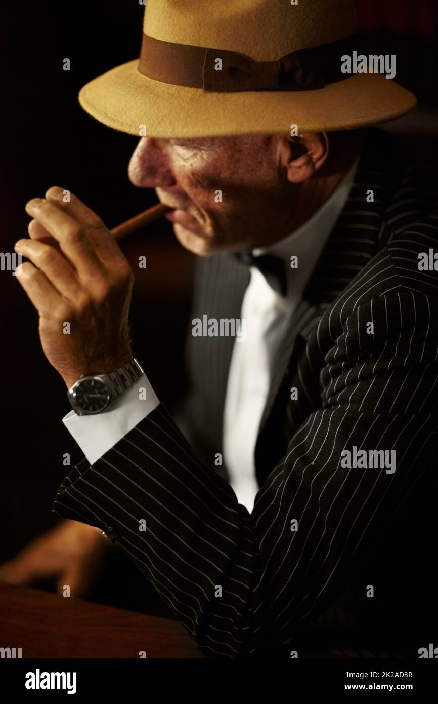 Leuchtet auf. Gealterter Mobboss, der einen Hut trägt und ernst aussieht, während er eine Zigarette anzündet. Stockfoto